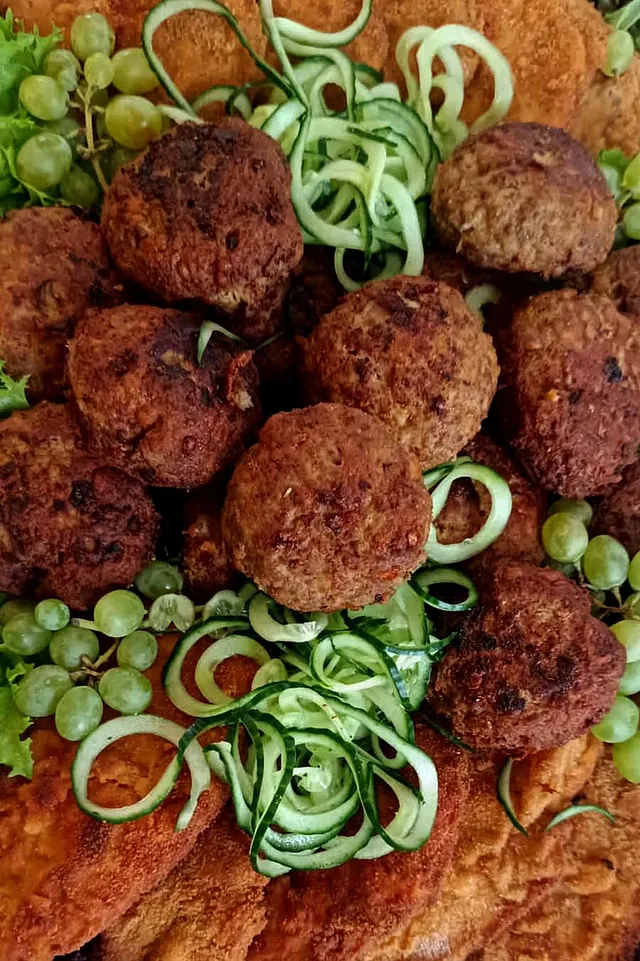 Fleischbällchen und Schnitzel angerichtet mit Gurkenstreifen und Trauben